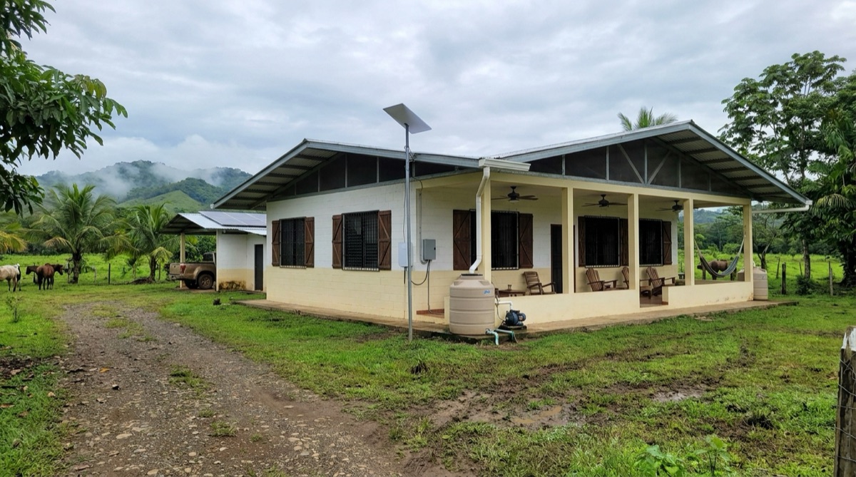 Die Außenseite von Stefans Haus in Panama, eine bescheidene Finca mit überdachter Terrasse, geparktem Fahrzeug, Pferden auf der Weide und nebligen Hügeln dahinter.